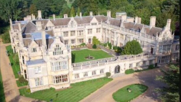 A large, historic mansion with a symmetrical facade, multiple chimneys, and a central courtyard.