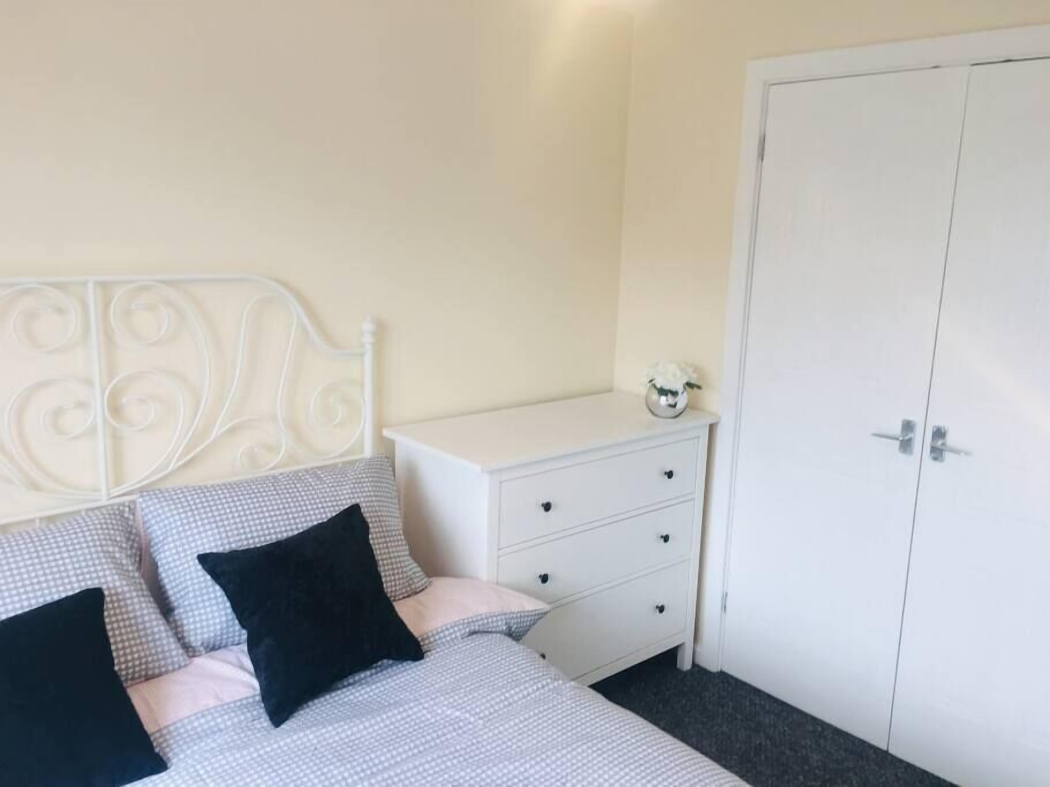 Une chambre à coucher avec un lit, une commode, une armoire et un petit vase posé sur la commode.