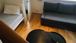 Une pièce comprenant un lit, un canapé gris, une petite table et une fenêtre avec des rideaux.