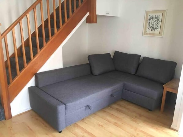 A grey sectional sofa with a wooden staircase and a framed picture on the wall.