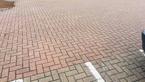 Une aire de stationnement dallée, avec une voiture blanche garée au premier plan.