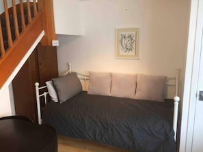 A small bedroom with a single bed, a wooden staircase, and a framed artwork on the wall.