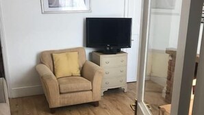Quarto com sofá bege, televisão sobre um móvel, quadro pendurado na parede e piso de madeira.