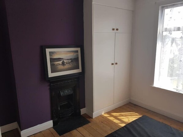 A room with a fireplace, a framed picture, a white wardrobe, and a window with a view.