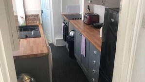 Uma cozinha compacta com bancada de madeira, geladeira preta e um cesto de lixo.