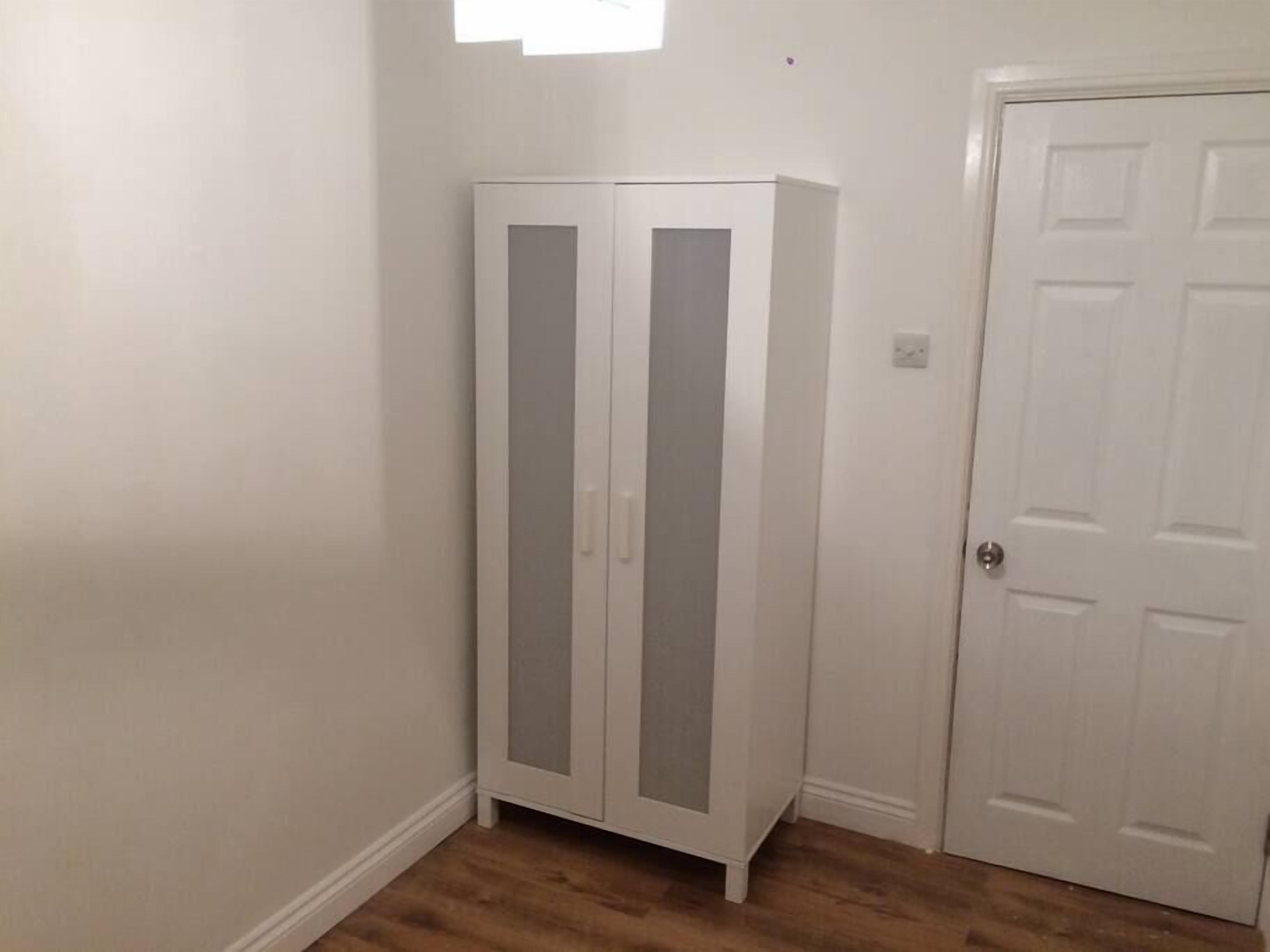 Une pièce avec une armoire blanche, une porte blanche et un plancher en bois.
