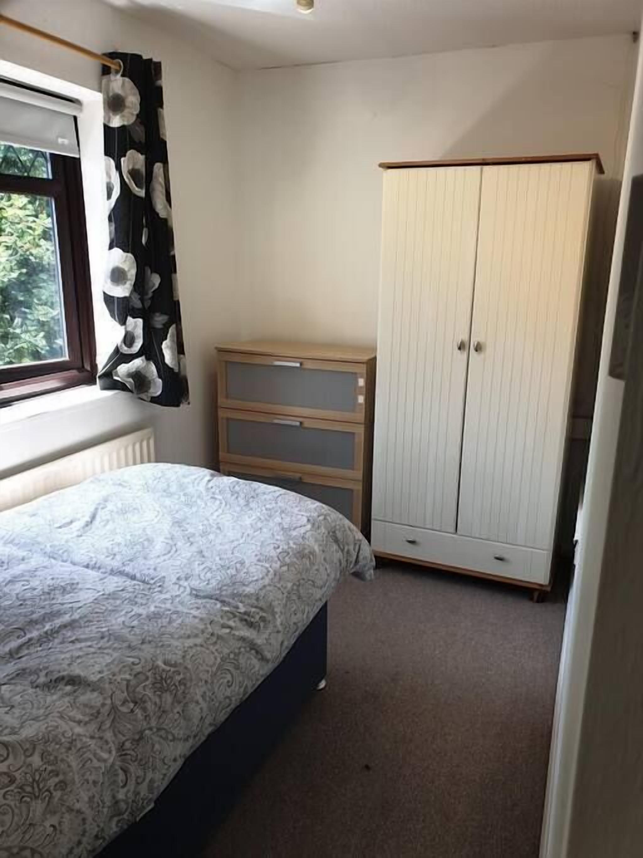 Ett sovrum med en säng, en garderob, en byrå och ett fönster med gardiner.