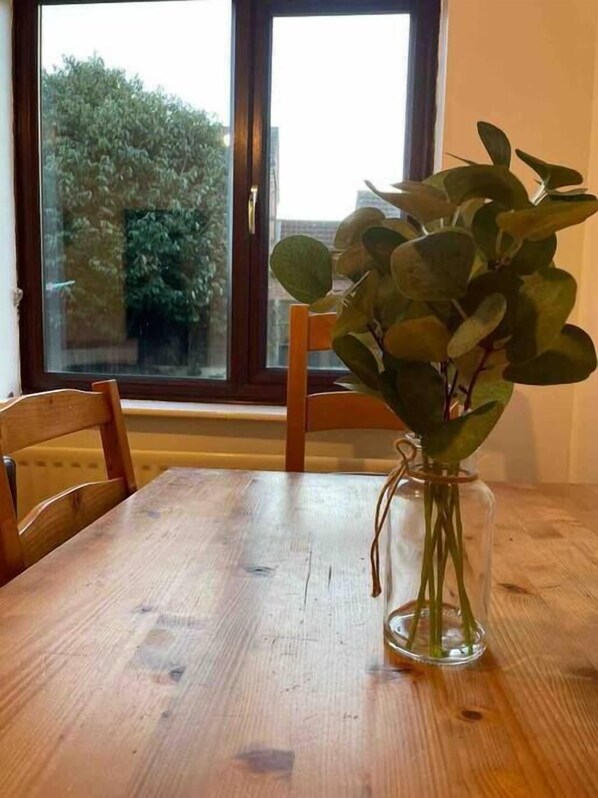 A wooden dining table with a clear glass vase containing green foliage.