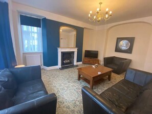 A living room with a fireplace, a television, and a chandelier. - London Road Corporate House (Northamptonshire)