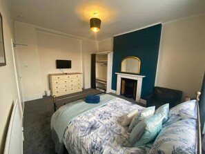 Ein Schlafzimmer mit Bett, Kommode, Fernseher, Kleiderschrank und Kamin.