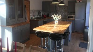 Eine moderne Küche mit Kochinsel, Barhocker, Pendelleuchten und einem Kühlschrank.