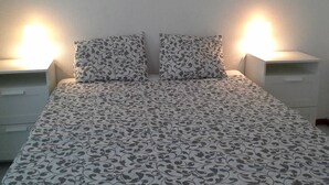 Un lit avec une couvre-lit à motifs, deux lampes de chevet et une table de chevet avec des tiroirs.