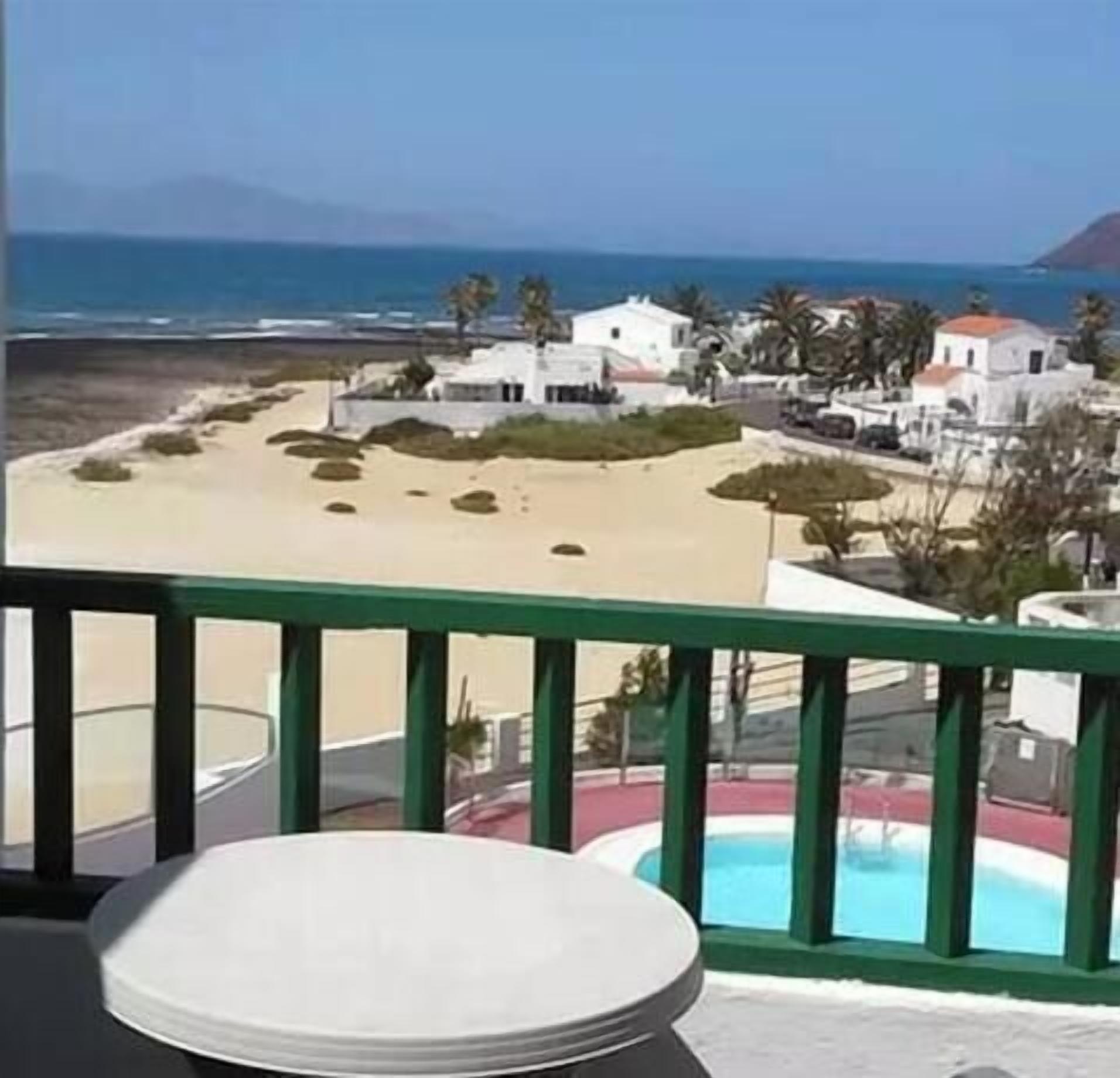 En balkong med utsikt över en strand, en pool och vita byggnader.