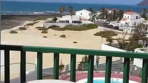 Un balcon avec vue sur une plage, une piscine et des bâtiments blancs.