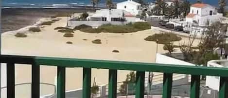 En balkong med utsikt över en strand, en pool och vita byggnader.