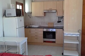 A compact kitchen with a microwave, oven, and sink, a small dining table with chairs, and a metal shelf unit.