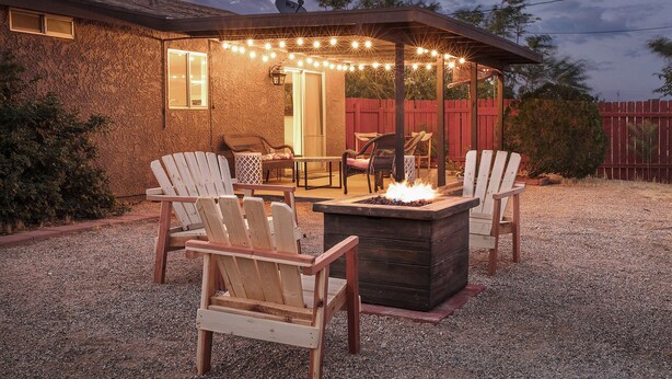 Um pátio externo com cadeiras Adirondack, uma lareira e luzes de corda.