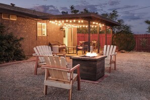 An outdoor patio with Adirondack chairs, a fire pit, and string lights. - Desert Oasis-Close to National Park, Views, FirePit, Family & Pet Friendly (Joshua Tree)