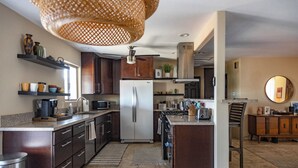 Uma cozinha moderna com armários de madeira escura, uma geladeira de aço inoxidável e uma área de refeições com mesa e cadeiras de madeira.