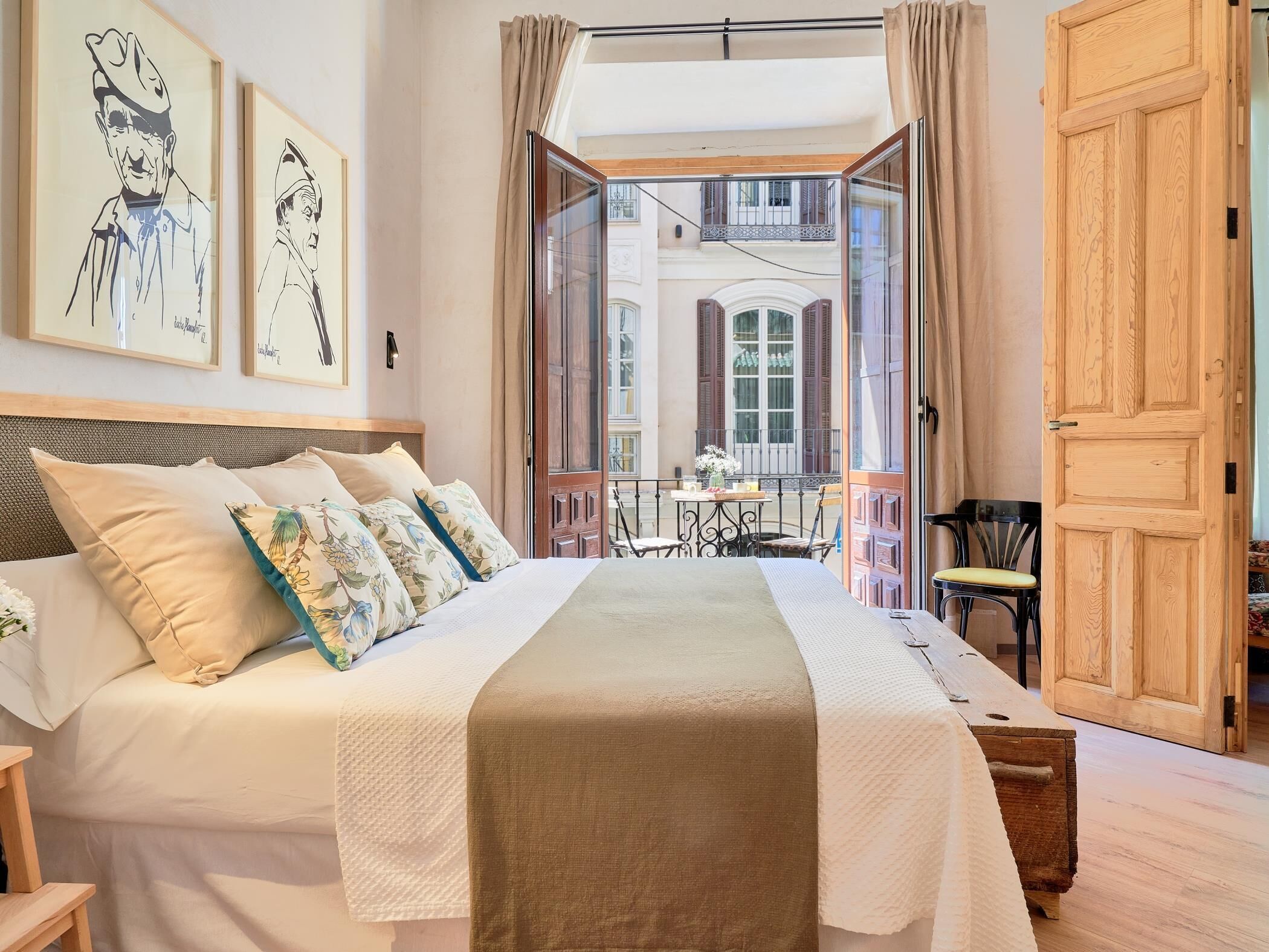 A bedroom with a large bed, a wooden door, and a balcony with a table and chairs.