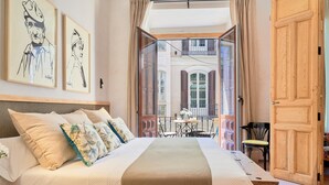 A bedroom with a large bed, a wooden door, and a balcony with a table and chairs.