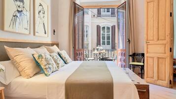 A bedroom with a large bed, a wooden door, and a balcony with a table and chairs.