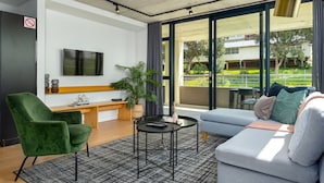 A modern living room with a green armchair, a grey sofa, a small round table, and a TV mounted on the wall. - FortyonL 709 (Cape Town)