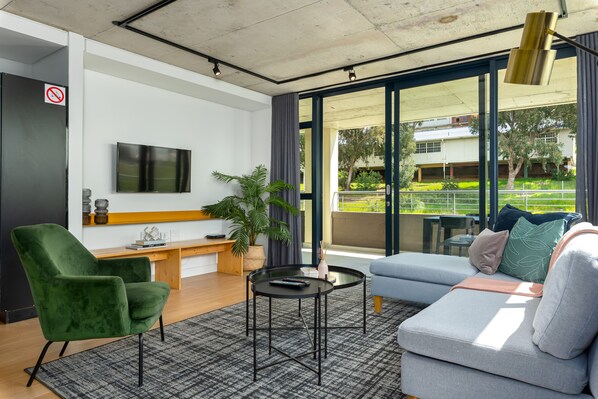 Un salon moderne avec un fauteuil vert, un canapé gris, une petite table ronde et un téléviseur fixé au mur.