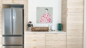 Eine Küche mit Holzschränken, einem Edelstahlkühlschrank, einem gewebten Korb, einer Topfpflanze und einem gerahmten Kunstwerk an der Wand.
