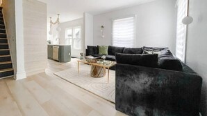 Ein modernes Wohnzimmer mit einer dunklen Couch, einem Couchtisch und einer Küche im Hintergrund.