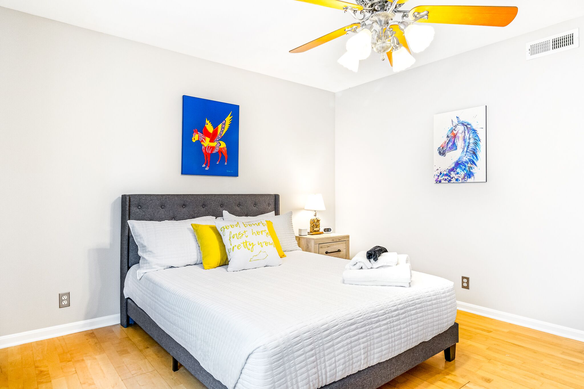 A bedroom with a bed, a nightstand, a lamp, and artwork on the walls.