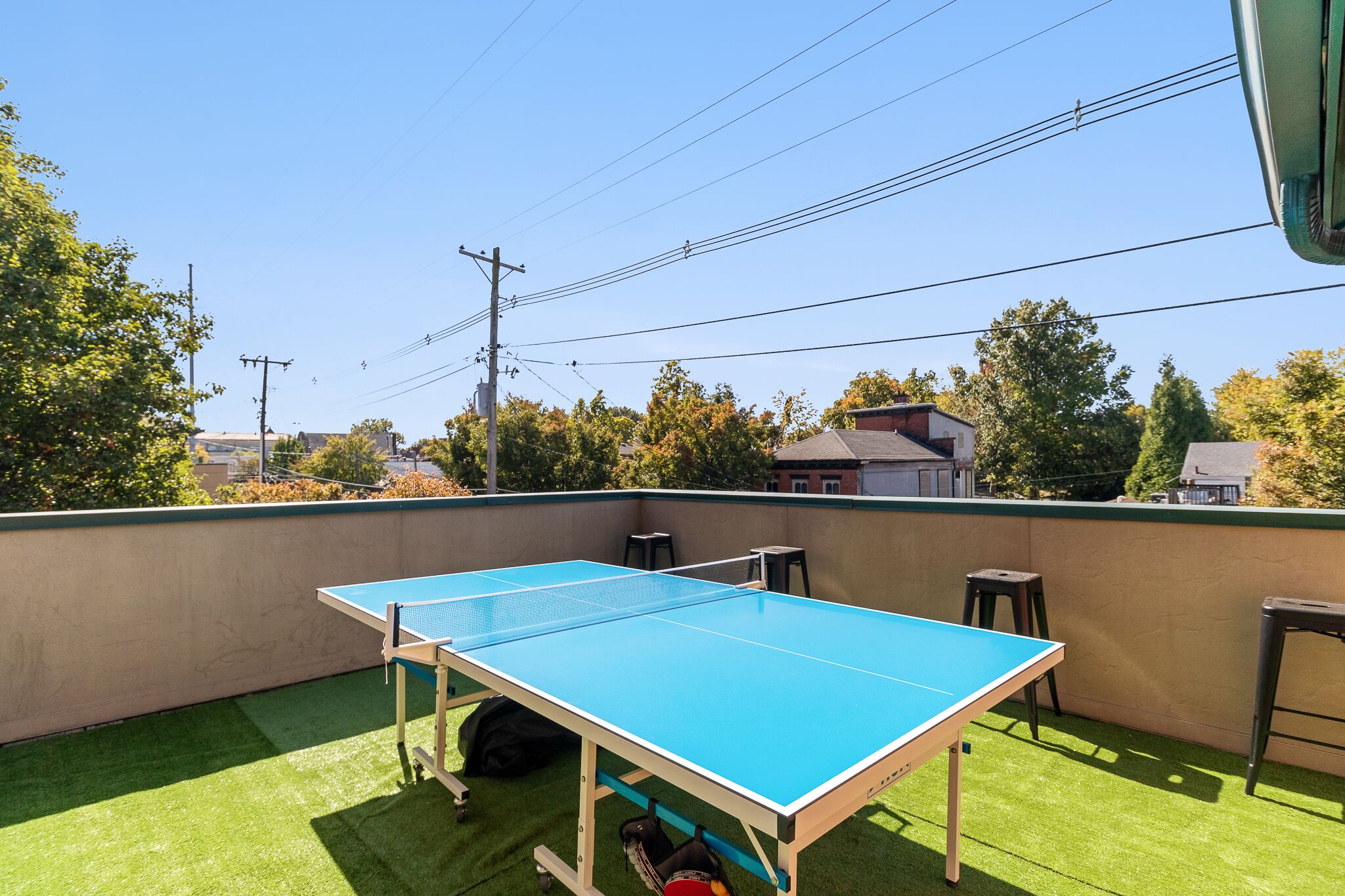 Een pingpongtafel op een buitenterras met kunstgras, omringd door een lage muur en een helder uitzicht op de omgeving.