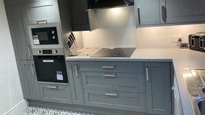 Una cocina compacta con muebles grises, horno empotrado, microondas y tostadora.