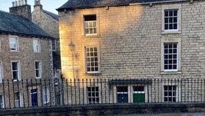 Un edificio de piedra con camino de grava y valla metálica.