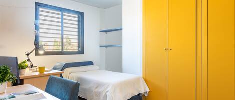 A dormitory room with a bed, desk, chair, and a yellow wardrobe.