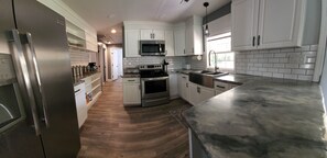 A modern kitchen with white cabinets, stainless steel appliances, and a wooden floor.