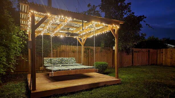En gyngestol i træ med pergola, lyskæder og en træterrasse.
