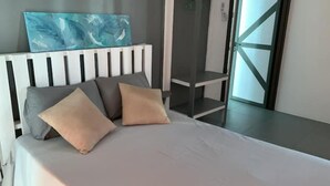 Een moderne slaapkamer met een wit hoofdeinde, een bed met beige en grijze kussens, een schilderij boven het hoofdeinde, en uitzicht op een glazen deur die naar buiten leidt.