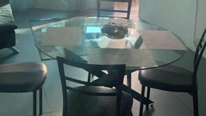 Een eethoek met een glazen tafel en stoelen, een bank en uitzicht op de omgeving door een groot raam.