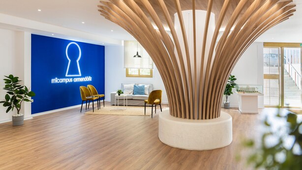 A modern reception area with a blue wall, wooden decorative structure, and seating. - Micampus Armendáriz - Students Residence (Seville)