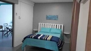A bedroom with a bed, a painting on the wall, and a desk with a chair in the adjacent room. - Apartment 1 Chambre Avec Balcon Face à la Plage (Flic en Flac)