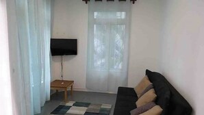 A living room with a black sofa, a small wooden table, a TV, and a checkered rug. - Apartment 1 Chambre Avec Balcon Face à la Plage (Flic en Flac)