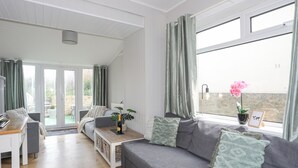 Een moderne woonkamer met een grijze bank, een houten salontafel en uitzicht op het landschap door grote ramen.