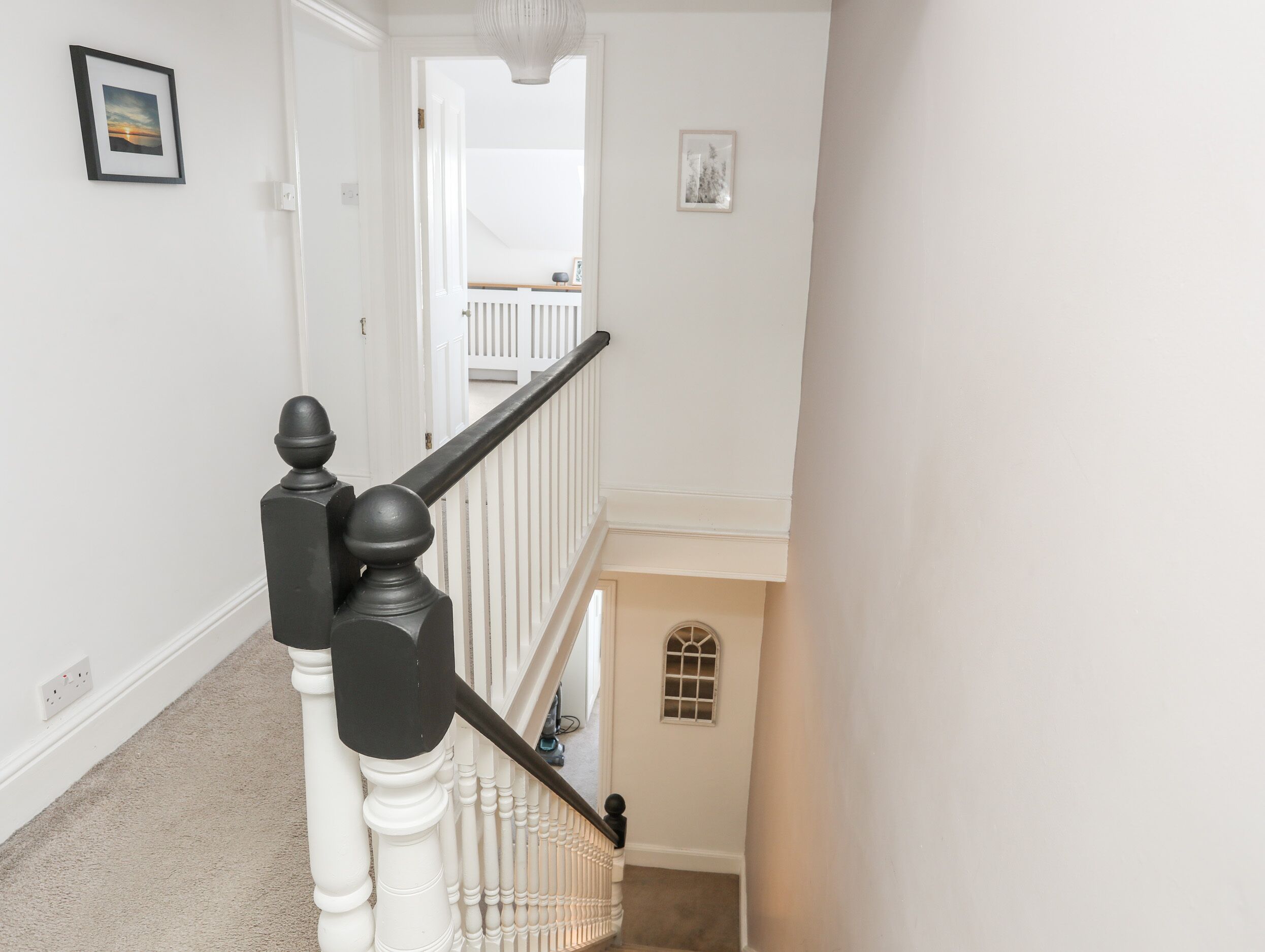 A staircase with white balusters and black handrails, leading to a landing with a white railing and a small window.