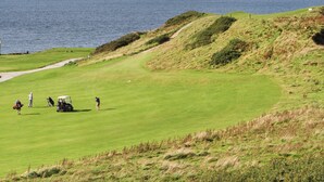 Een golfbaan met uitzicht op zee, een pad dat naar het water leidt, en enkele personen en golftrolleys.