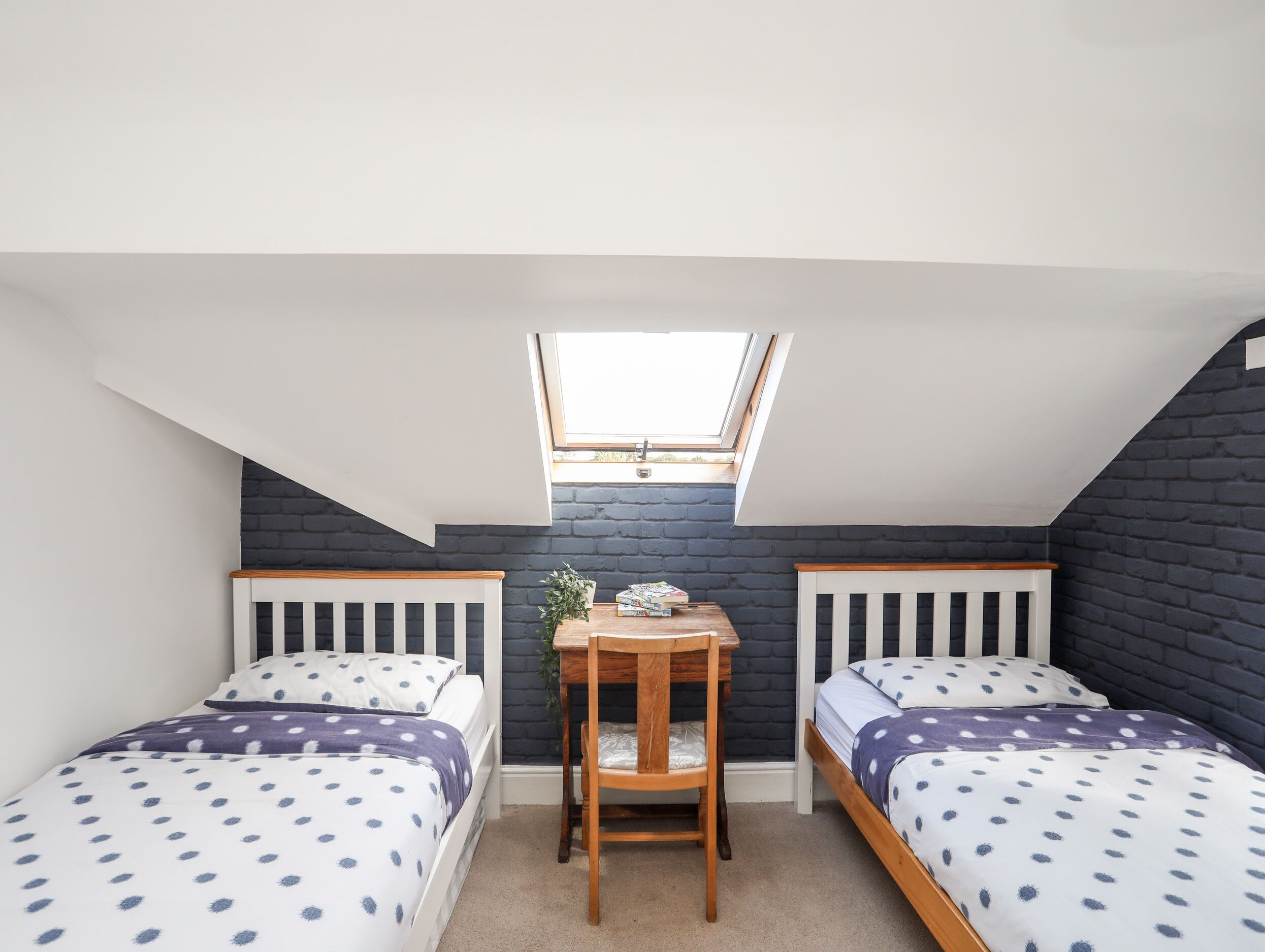 A small, well-lit room with two single beds, a wooden table, and a skylight.