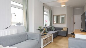 Een moderne woonkamer met twee grijze banken, een houten salontafel, een televisie en een grote spiegel.