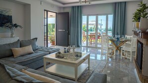 A modern living room with a sofa, coffee table, and dining area with chairs. - Villa Mediterranean Oasis (Rethymno)