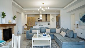 A modern living room with a sectional sofa, a white coffee table, and a fireplace. - Villa Mediterranean Oasis (Rethymno)