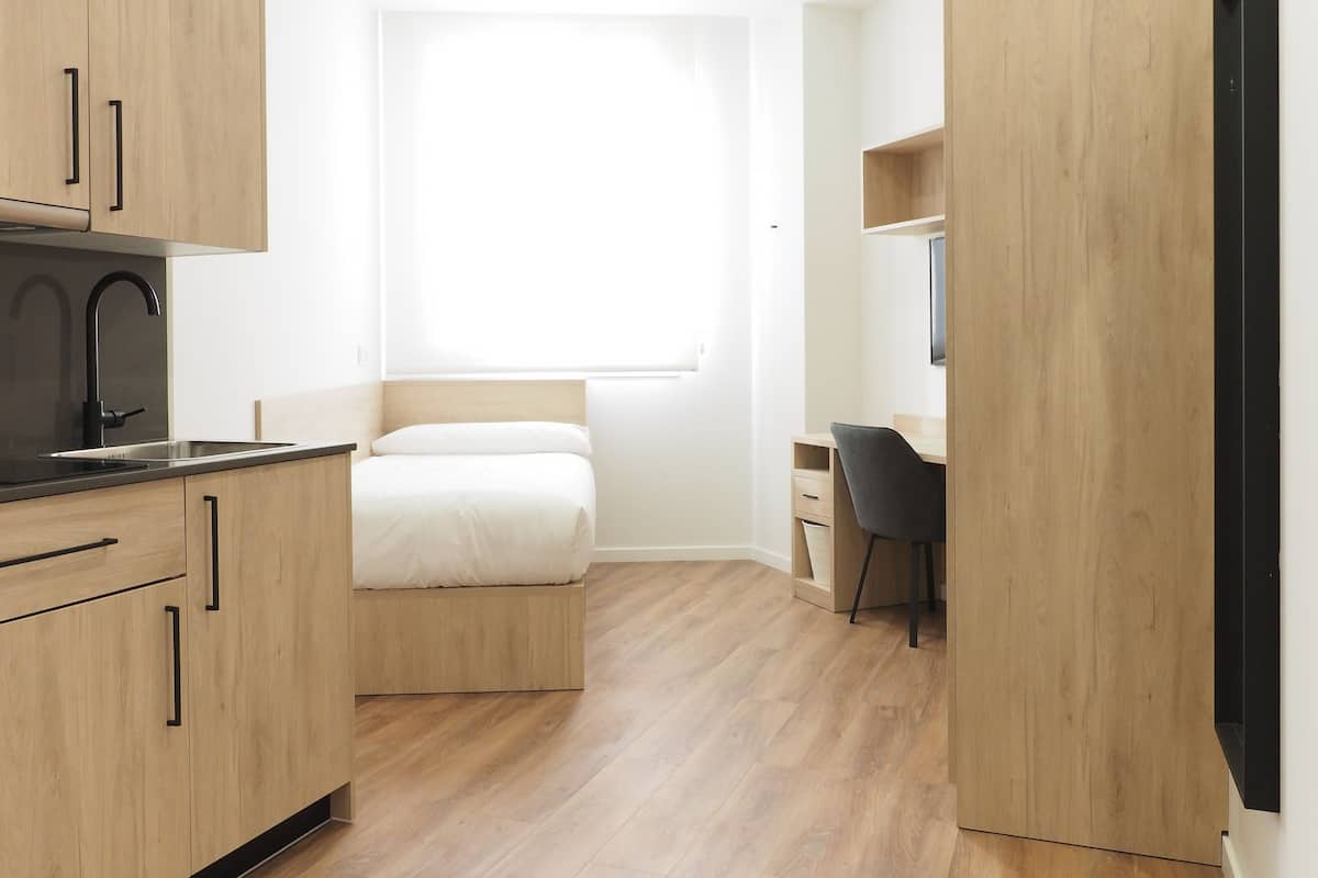 A compact room with a bed, a desk, and a kitchenette.